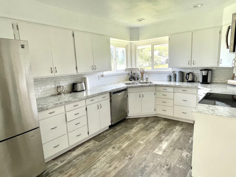 A kitchen with white cabinets and wood floors.