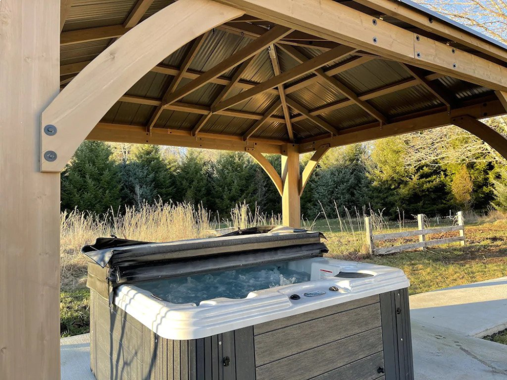 A hot tub under a wooden structure in the middle of a park.