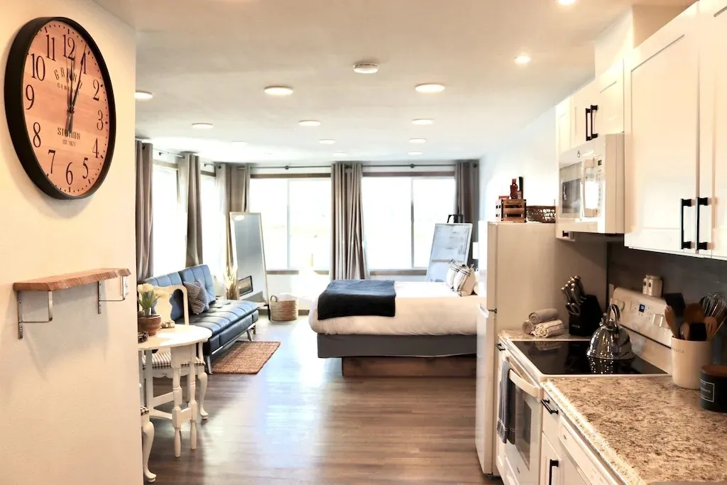 A kitchen and living room with a bed in the background.