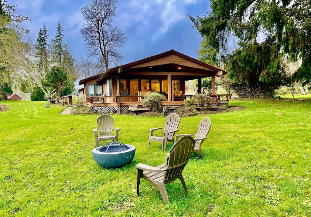 A group of chairs in the grass near a fire pit.